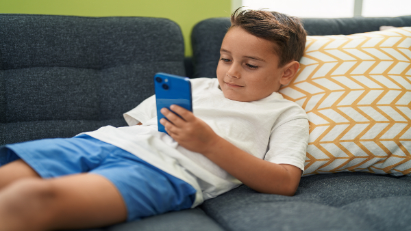 child-using-smartphone-lying-sofa-home