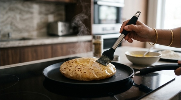 A golden puran poli being cooked on a modern black non-stick tawa