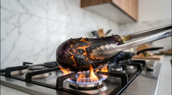 Roasting a large purple eggplant over an open gas flame with garlic cloves inserted