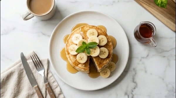 A stack of soft fluffy breakfast banana pancakes topped with maple syrup and fresh banana slices