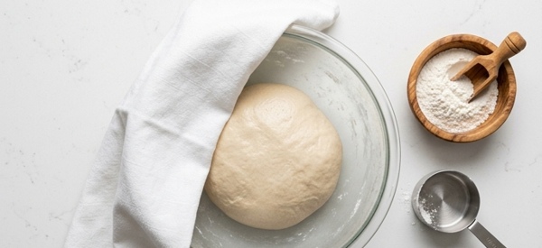 Close up of hands kneading soft wheat dough in a modern glass bowl