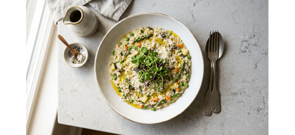 A creamy bowl of vegetable risotto topped with fresh herbs and parmesan cheese