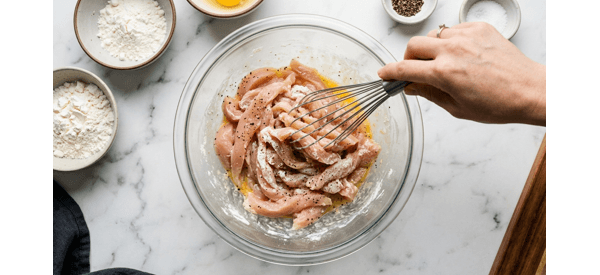 Coating chicken strips with flour and egg mixture in a glass bowl