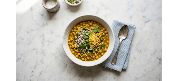 A steaming bowl of Kolkata Street Special Ghugni garnished with onions and lime