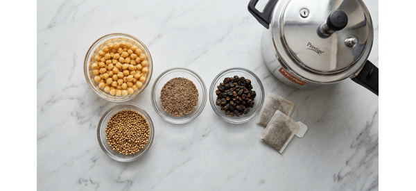 Soaked chickpeas next to whole spices and tea bags on a marble counter