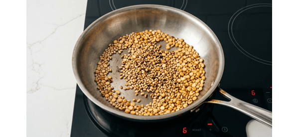 Urad dal and chana dal being dry roasted in a modern stainless steel pan